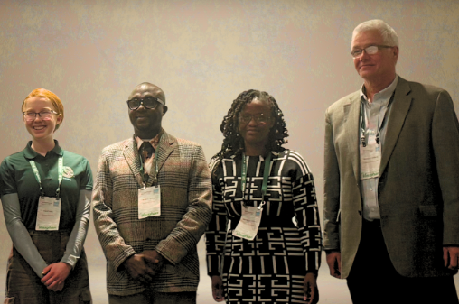 Three graduate students stand with their professor after winning awards.